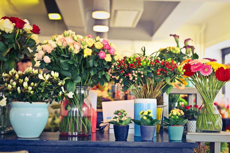 A display of various fresh flower arrangements in an indoor floral shop, featuring large bouquets with pink, white, and red roses arranged in clear glass vases and ceramic pots, complemented by smalle