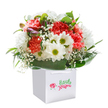 This cheerful bouquet, thoughtfully arranged by Flowers Collier Row, seems to gather the joyful atmosphere of the RM5 area into one delightful package. Ruffled coral and radiant red carnations form a lush, tactile centrepiece, softened by snowy-white daisies whose bright yellow-green centers shine like welcome beacons through a garden gate. Dainty sprays of baby's breath drift gently among the blooms, infusing the bouquet with a touch of innocence and lightness that calls to mind family picnics at Lawns Park. Along one edge, hints of unopened purple-tinged buds suggest the quiet excitement of something new beginning, their presence lending a subtle intrigue. Framing it all, a cascade of glossy, deep green leaves evokes the well-cared-for green spaces and gardens that Collier Row is known for. The structured, square white gift bag, topped with neat ribbon handles, speaks to the care and ease of local gifting-perfect for a bright birthday morning or a heartfelt thank-you shared with a neighbour. Soft, even lighting highlights each hue and delicate petal, amplifying the bouquet's sincere, uplifting spirit and making it a cherished gift for any occasion in Collier Row.
