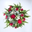 Viewed from directly above against a clean white background, this generous bouquet appears as a lush, circular tapestry of red, white, and fresh green, the kind of hand-tied arrangement you might see carried out of a Collier Row florist on a bright afternoon. At its heart are velvety crimson roses, some still in tight bud, others beginning to unfurl in soft spirals of petals, giving the whole design a romantic, almost heartbeat-like focus. Nestled closely alongside are ruffled carnations in deep fuchsia and ruby red, their frilly edges catching the light and adding a joyful, almost party-like texture. Clusters of small, daisy-like white spray chrysanthemums are dotted throughout, their crisp petals and golden centres bringing a cheerful brightness and gentle balance to the richer tones. Tiny stars of white gypsophila drift between the larger blooms, like a fine floral mist, softening every transition and lending an airy, dreamlike quality. The flowers are cradled and framed by layers of greenery: strong, pointed dark green leaves that give structure and direction to the bouquet, and rounded, silvery eucalyptus leaves that weave in and out, offering cool blue-green notes and suggesting a clean, herbal fragrance. The overall impression is of fullness and movement, as if the bouquet is gently expanding from its centre. This arrangement feels perfect for an anniversary, a Valentine's surprise, or a heartfelt thinking of you sent to a home near Collier Row's quiet residential streets, a bouquet that would light up a kitchen table or living room with colour, freshness, and sincere affection.