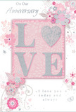 This close-up image captures an anniversary card whose delicate design evokes the soft romance of a carefully chosen floral gift delivered across Collier Row. The centre of the card is dominated by the word LOVE, spelled in tall, raised letters that glisten with a fine dusting of glitter. The textured surface of these letters looks slightly rough yet refined, inviting the fingertips to linger. They rest on a blush-pink panel that appears subtly raised from the rest of the card through gentle shading, adding a layered, almost three-dimensional quality to the composition. Around this central word, a ring of stylised flowers and curling vines spreads gracefully. The blossoms are drawn in fine lines and soft washes of blush pink, pearly white, and silver-grey, their petals slightly overlapping like flowers placed with care in a romantic bouquet. Slender stems and swirling tendrils curl around them, filling the space without overwhelming it, much like the balanced greenery in an anniversary arrangement. The background is a soft, powdery pink that enhances the serenity of the design and echoes the gentle tones often seen in pastel floral displays. Discreet touches of silver detailing catch the eye, giving the card a luminous, celebratory feel. An anniversary message appears in an elegant, script-like font that flows smoothly across the card, echoing the curves of the vines and petals. The overall impression is one of intimacy and enduring affection, as if the card itself were a paper embodiment of years of shared love and quiet moments spent together in and around the familiar streets and homes of Collier Row.